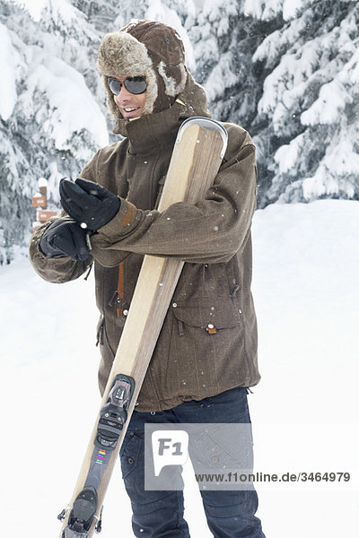 Junger Mann mit Skiern beim Anziehen der Handschuhe