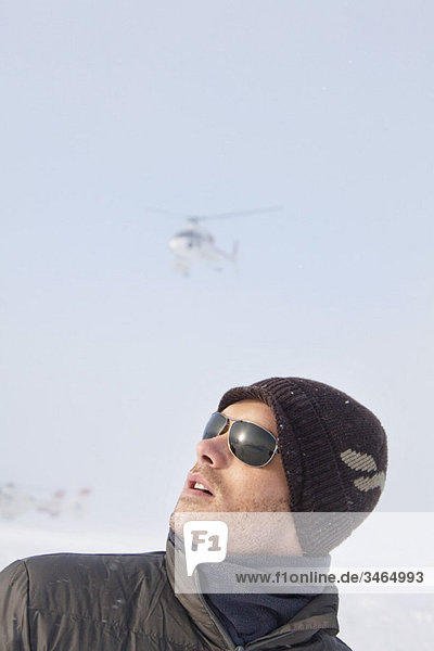 Portrait of young man in winter clothes looking up  helicopter in background