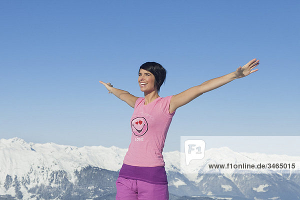 Junge lächelnde Frau mit erhobenen Armen  Berge im Hintergrund