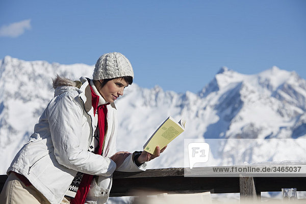 Junge Frau liest ein Buch  genießt Wintersonne  Berge im Hintergrund