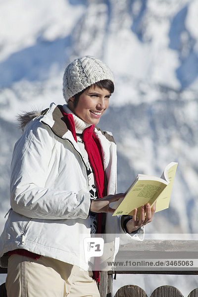 Junge Frau liest ein Buch  genießt Wintersonne  Berge im Hintergrund