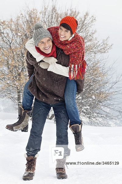 Junger Mann gibt seiner Freundin Huckepack im Schnee