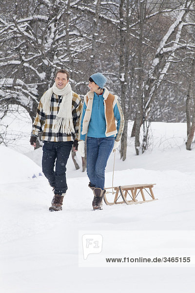 Junges Paar  das im Schnee läuft und einen Schlitten zieht.