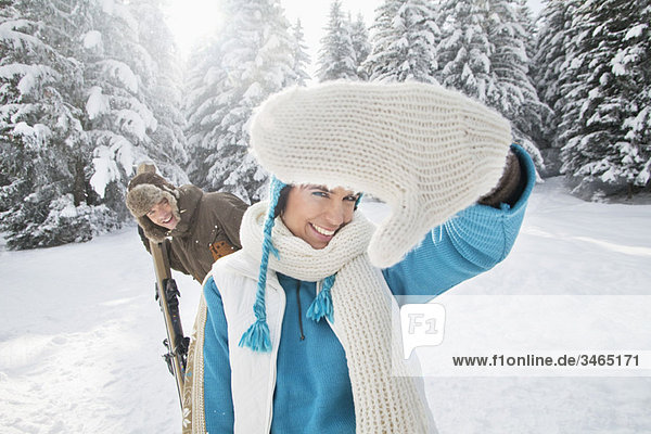 Young woman in winter clothes smiling at camera  man holding skis in background