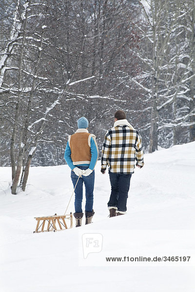 Young couple walking in snow pulling a sled  rear view