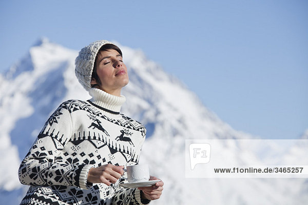 Young woman with coffee cup  enjoying winter sun  mountains in background