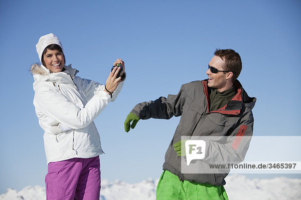 Junge Frau in Skibekleidung beim Fotografieren ihres Freundes
