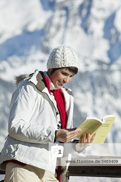 Young woman reading a book  enjoying winter sun  mountains in background