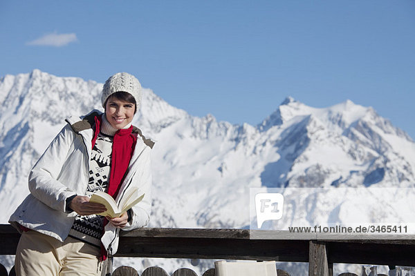 Young woman reading a book  enjoying winter sun  mountains in background