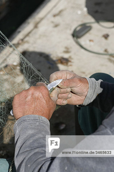 Ein Fischer schneidet ein Fischernetz und konzentriert sich auf die Hände.