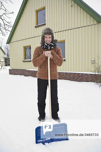 A man leaning on a snow shovel preparing to shovel snow