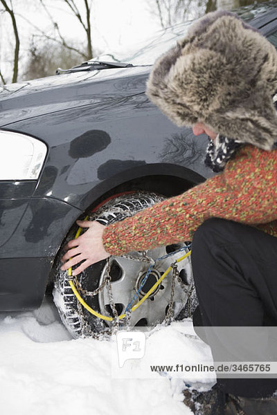 Ein Mann  der Schneeketten auf seine Reifen legt.
