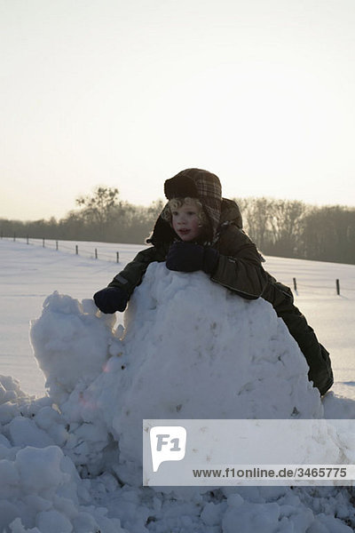 Ein Kind  das sich gegen einen Haufen Schnee lehnt.