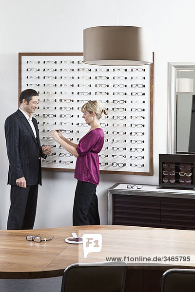 An optician holding up glasses to a man in an eyewear store