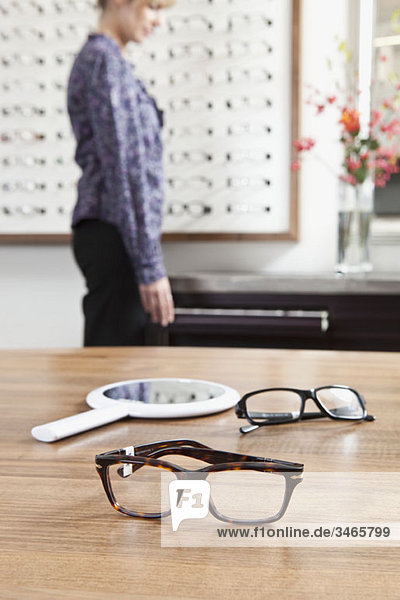 Zwei Brillen (eine im Fokus) in einem Brillengeschäft  Frau im Hintergrund