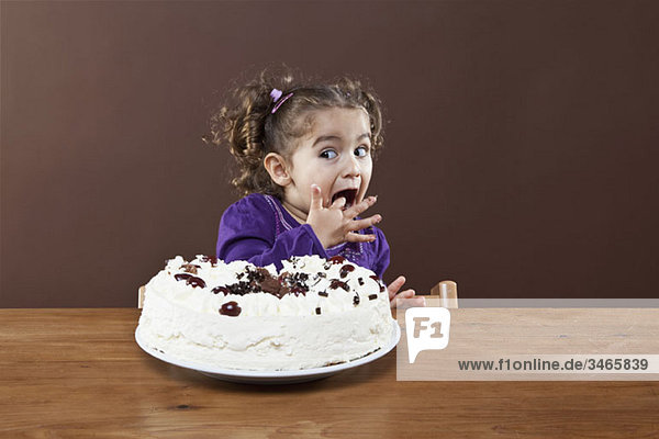 Ein junges Mädchen  das einen Geschmack von einem gefrosteten Kuchen schmuggelt.