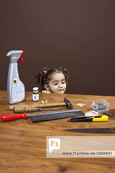 Ein junges Mädchen  das gefährliche Gegenstände auf einem Tisch betrachtet  Studioaufnahme