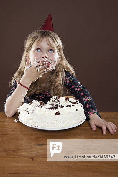 Ein Mädchen mit einem Partyhut  das Kuchen mit den Händen isst  Studioaufnahme
