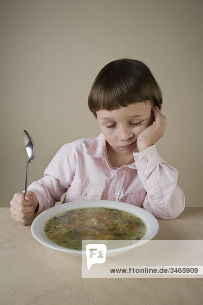 A boy looking disappointedly at a bowl of vegetable soup
