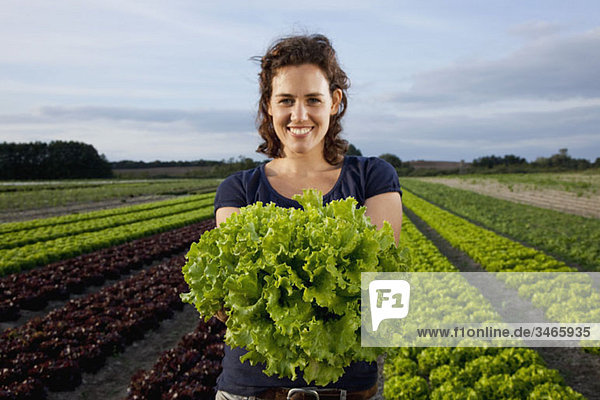Eine Frau hält einen frischen Salat auf einem Feld.