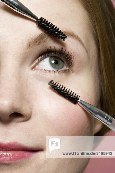 Eine Frau mit zwei Wimperntuschestäbchen  extreme Nahaufnahme des Gesichtes