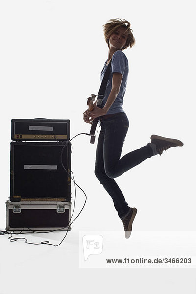 Eine Frau springt beim Spielen einer E-Gitarre  Studioaufnahme  weißer Hintergrund  hinterleuchtet