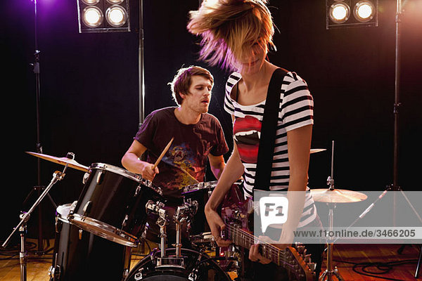 Ein Mann spielt Schlagzeug und eine Frau spielt Gitarre in einer Rockband auf der Bühne.