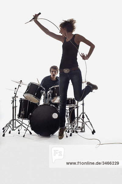 Eine Sängerin springt und ein Mann am Schlagzeug spielt  Studioaufnahme  weißer Hintergrund  hinterleuchtet