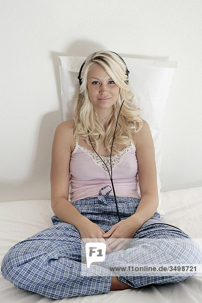 Portrait einer jungen Frau in Pyjamas sitzen auf dem Bett Musikhören mit Kopfhörern