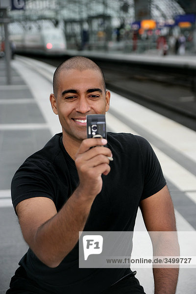 Man at railway station taking a picture with his mobile phone