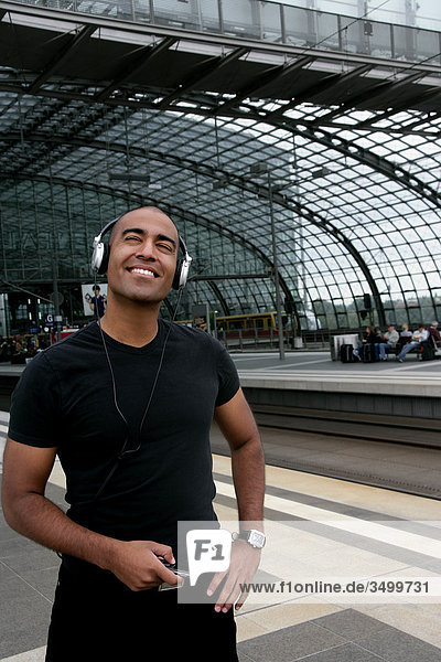 Mann mit MP3-Player und Kopfhörern auf einem Bahnsteig