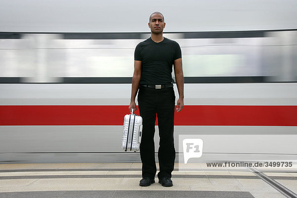 Mann mit Koffer auf einem Bahnsteig vor einem Zug  Frontalansicht
