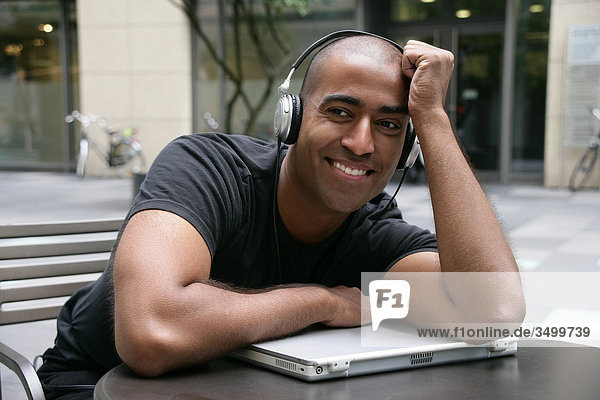 Mann mit Kopfhörern lehnt auf einem Notebook