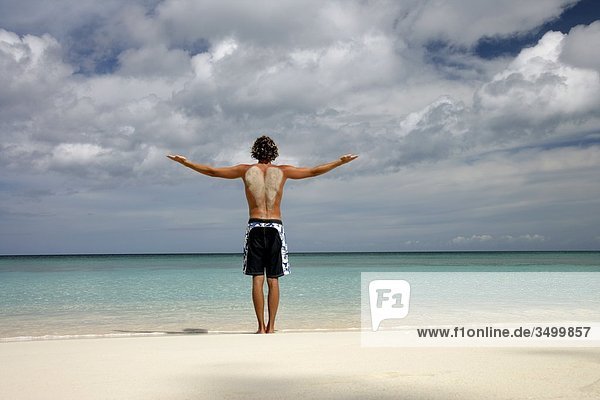 Mann mit ausgebreiteten Armen am Strand stehend  Paradise Island  Bahamas  Rückansicht