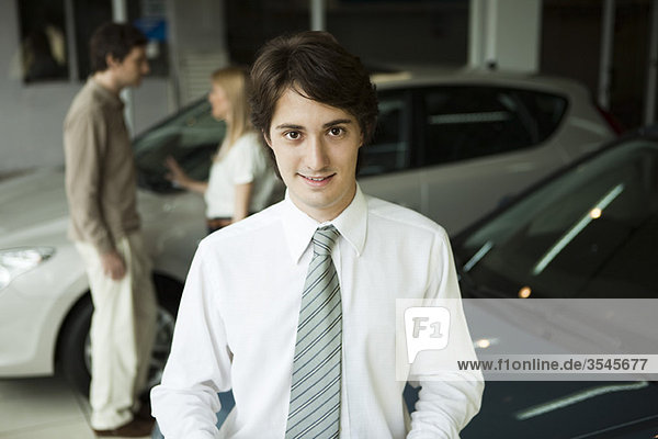 Autoverkäufer im Autohaus  Interessenten im Hintergrund