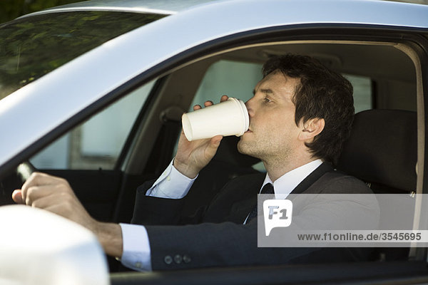 Mann trinkt Kaffee beim Autofahren