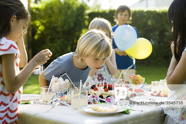 Boy blowing candles on birthday cake at outdoor birthday party