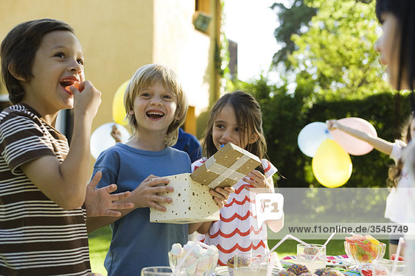 Boy opening gift and smiling with pleasure at birthday party