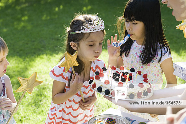 Mädchen bläst Kerzen auf Geburtstagskuchen bei einer Geburtstagsparty im Freien aus.