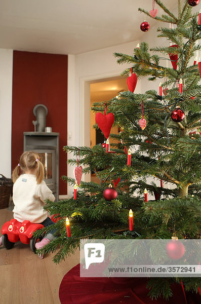 Weihnachtsbaum und Mädchen auf Bobbycar im Wohnzimmer