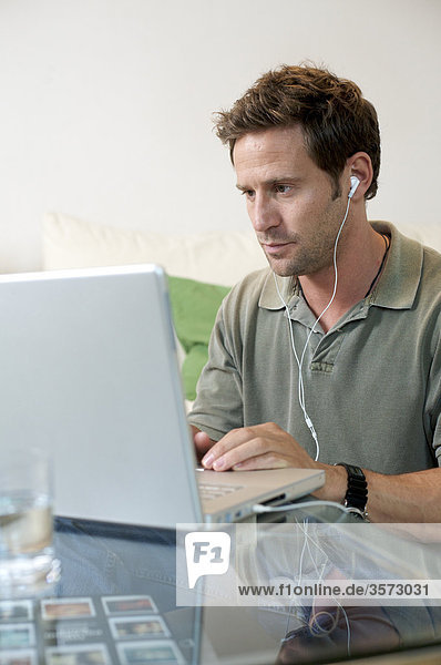 Mann mit Ohrstöpseln benutzt Laptop