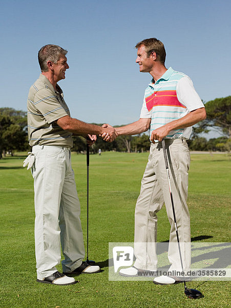 Two mature men shaking hands on golf course