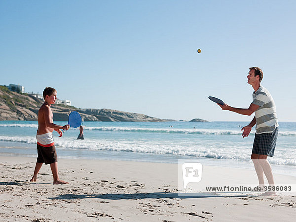 Father and son on playing paddleball on beach