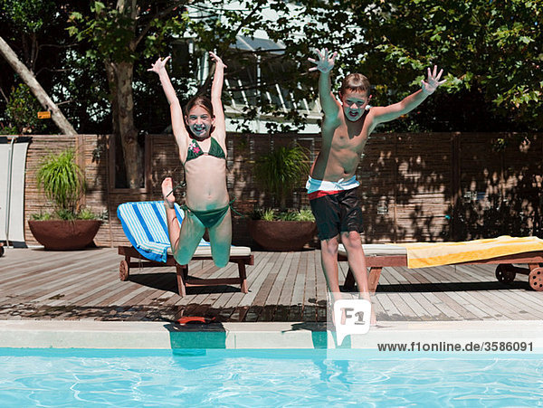 Boy and girl jumping into swimming pool