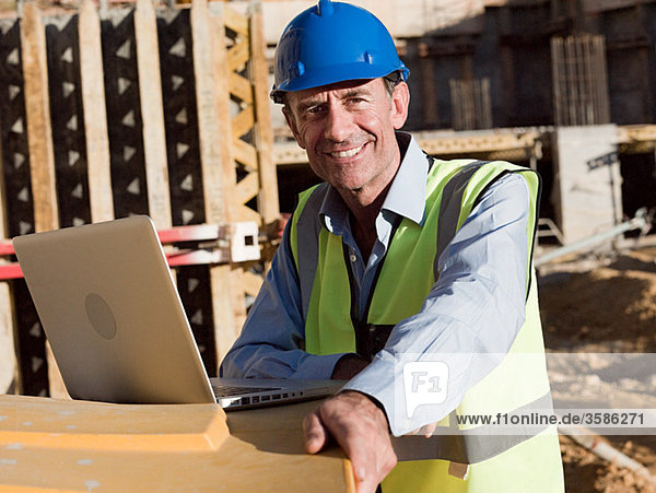 Erwachsener Mann mit Laptop auf der Baustelle