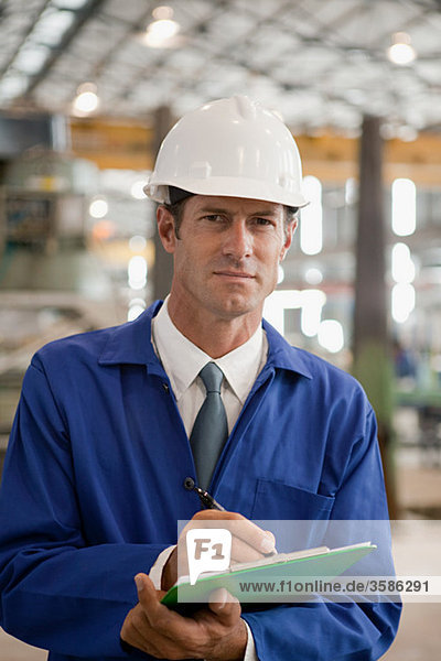 Erwachsener Mann mit Klemmbrett in der Fabrik