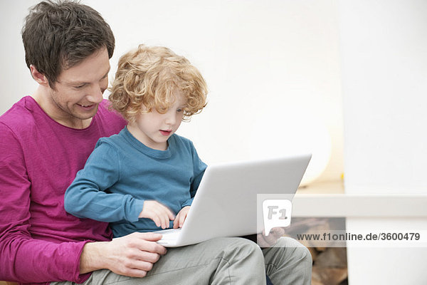Close-up of a man assisting his son in using a laptop
