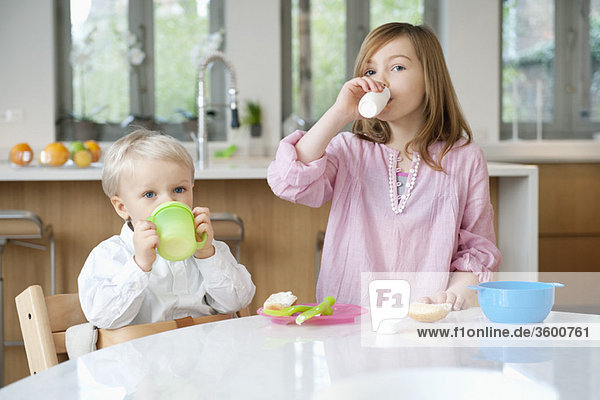 Girl drinking milk with her brother drinking juice at a breakfast table