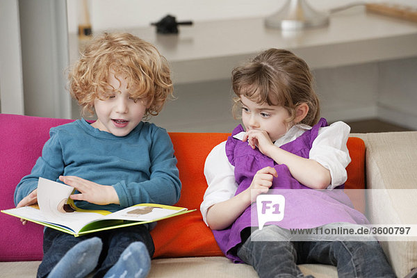 Junge sitzt mit seiner Schwester und liest ein Buch.