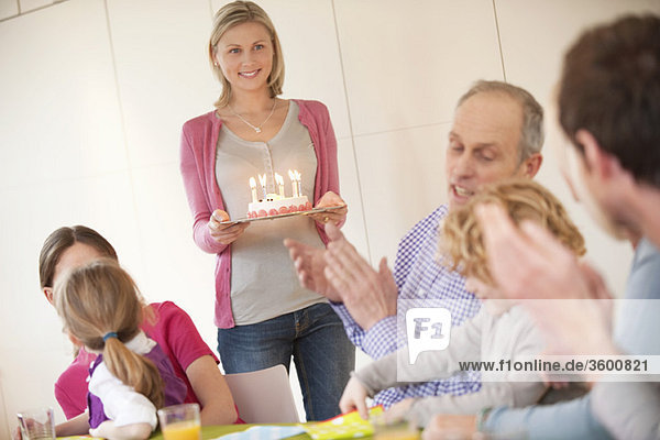 Familie bei einer Geburtstagsfeier mit einer Frau mit Kuchen im Hintergrund